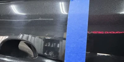 Black vehicle paint showing a taped section comparing corrected and uncorrected finish.
