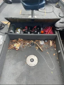 Open storage compartment under a bass boat's casting deck, showing tackle boxes and fishing gear.