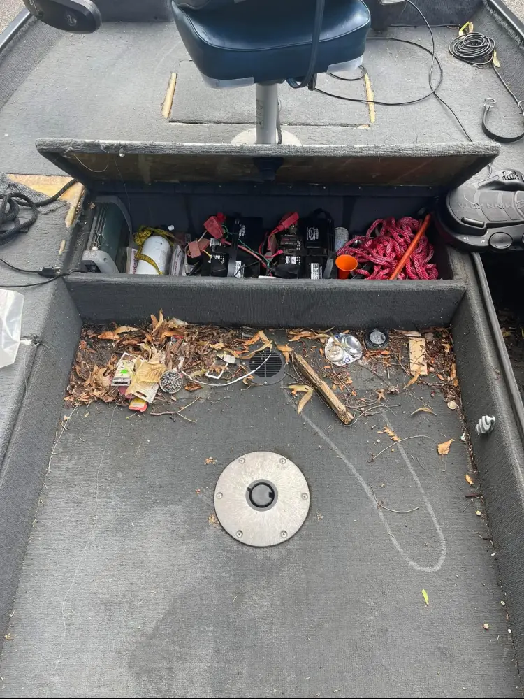 Open storage compartment under a bass boat's casting deck, showing tackle boxes and fishing gear.