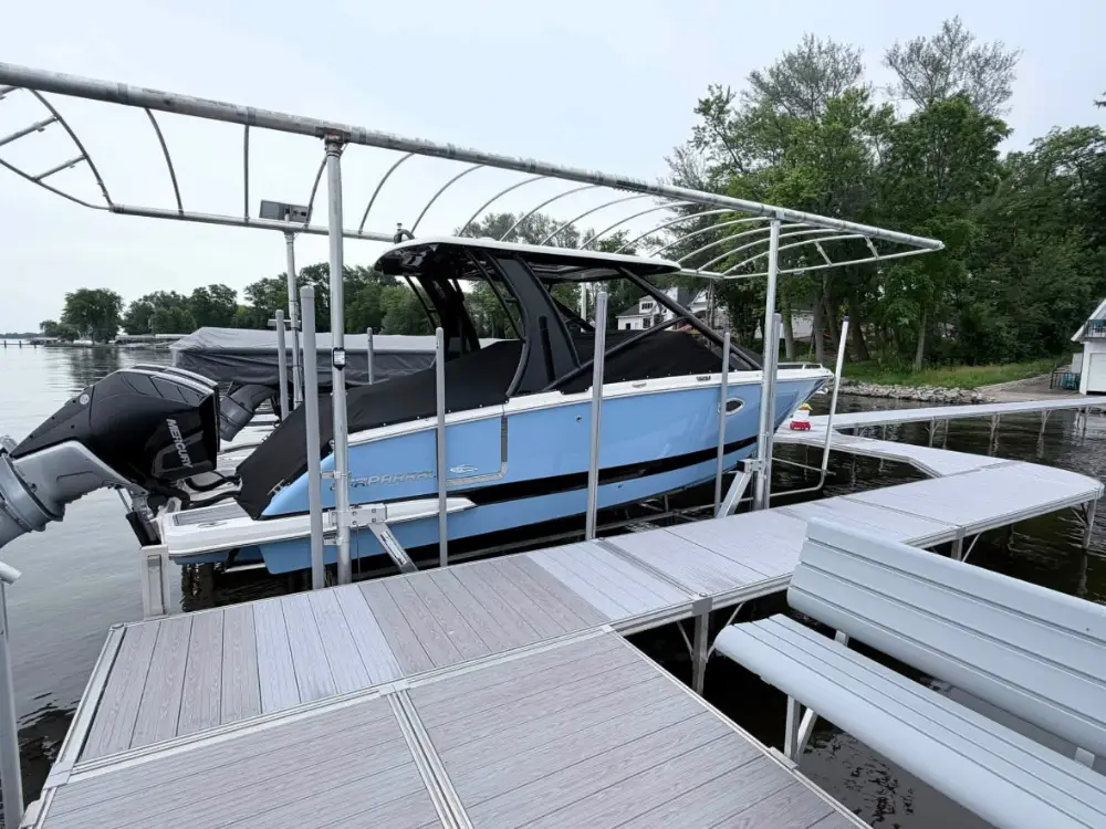 Blue and white powerboat secured to an aluminum slip dock on the water with a bench visible.