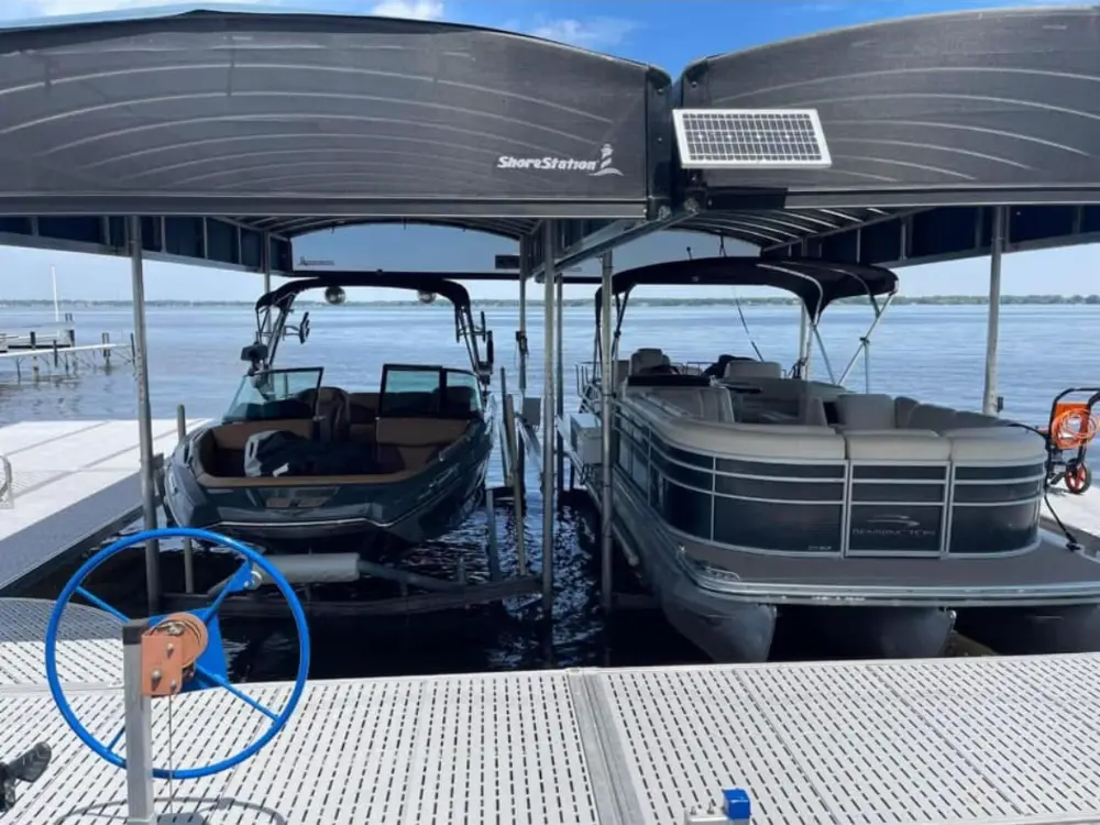 Two boats parked in lifts under a covered dock on a calm lake, viewed past a white pier deck.