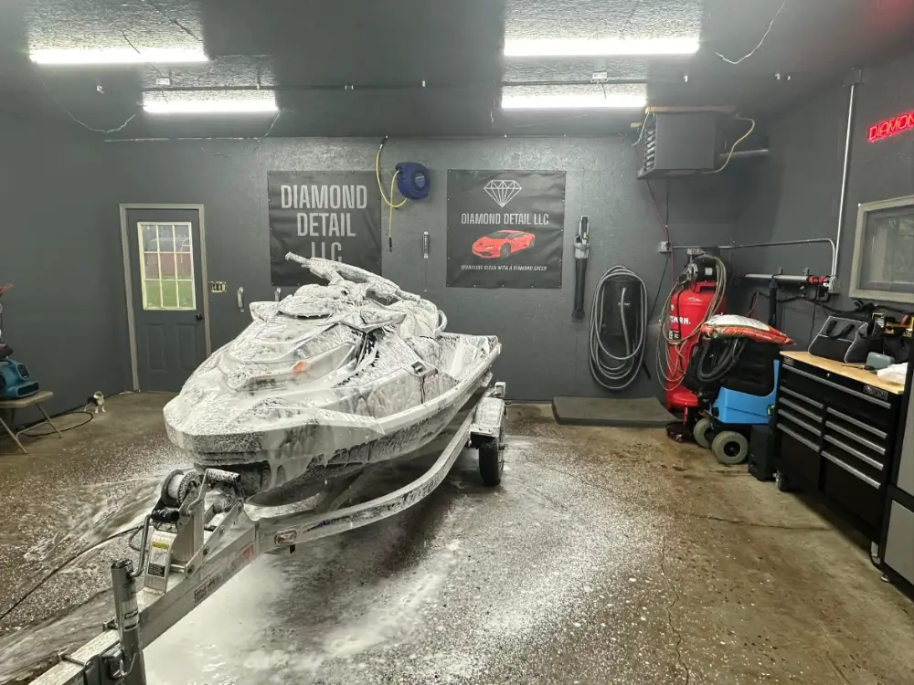 Personal watercraft covered in wash soap and foam on a trailer inside an automotive detail shop.