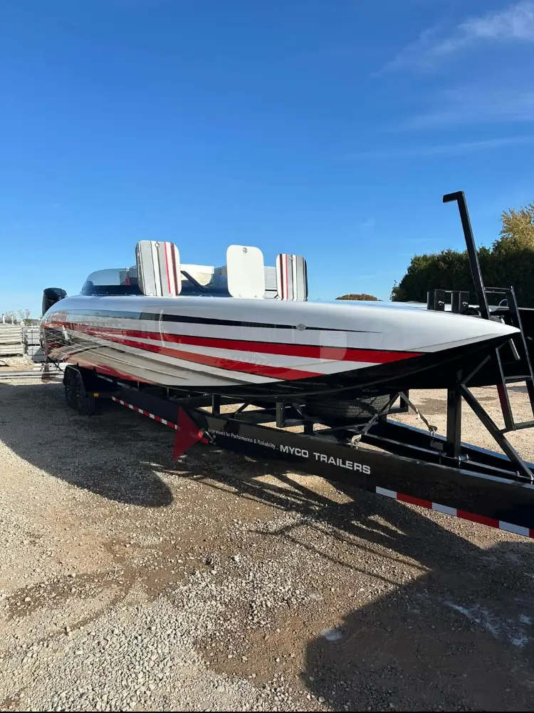 Side profile of a high-performance bass boat on a trailer, with red and white graphics, parked in an outdoor lot.