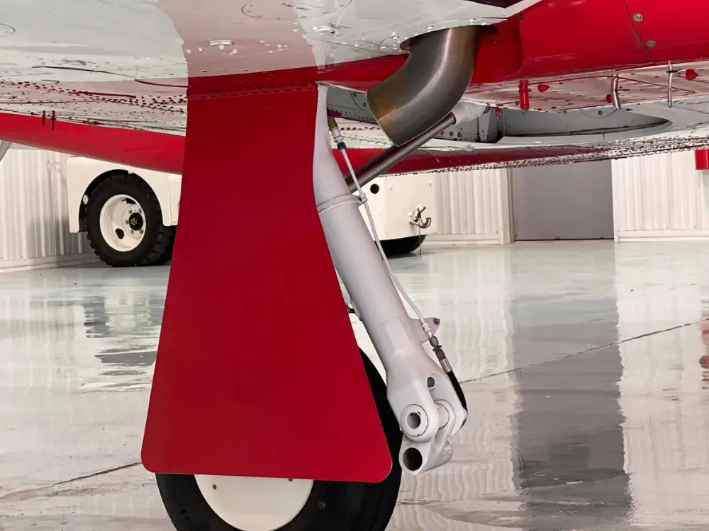 Close-up view of the nose landing gear and red wheel fairing on a red and white airplane inside a hangar.
