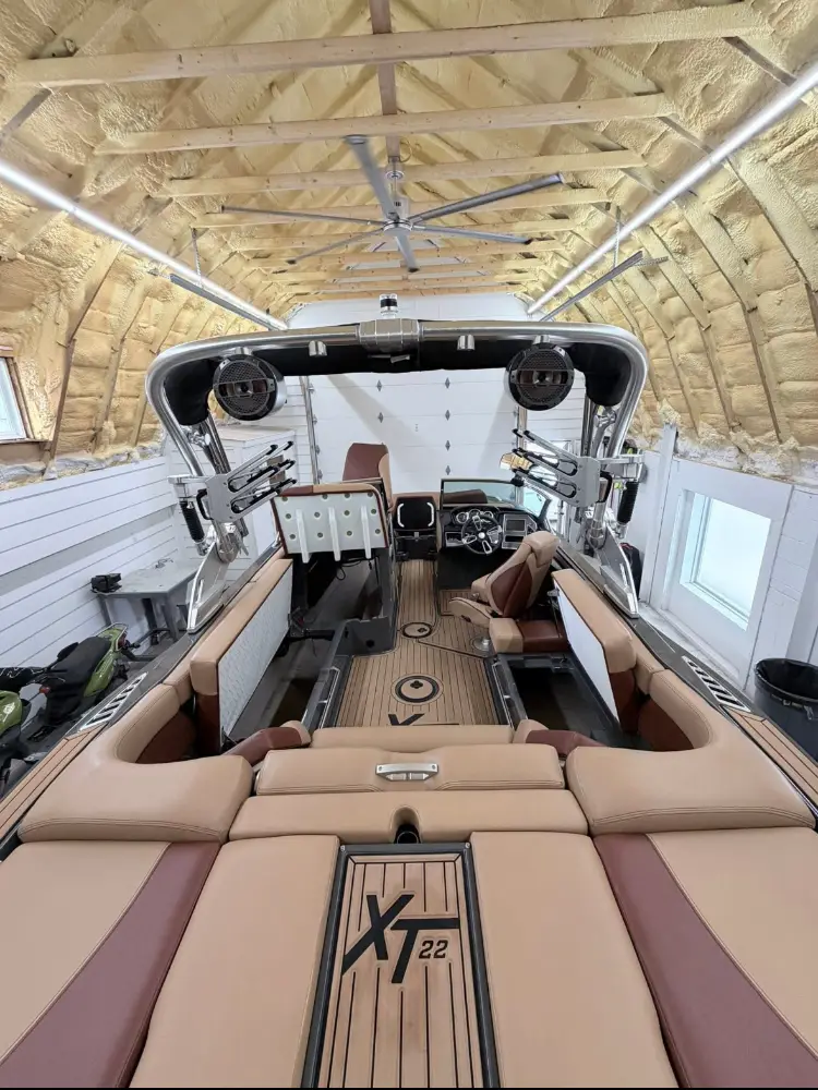 View from the aft of a luxury wakeboard boat, showing detailed brown and white seating and a tower, inside a boat storage facility.
