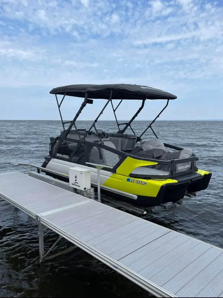Yellow and black pontoon boat with a bimini top, tied to an aluminum dock on a large lake under a blue sky.
